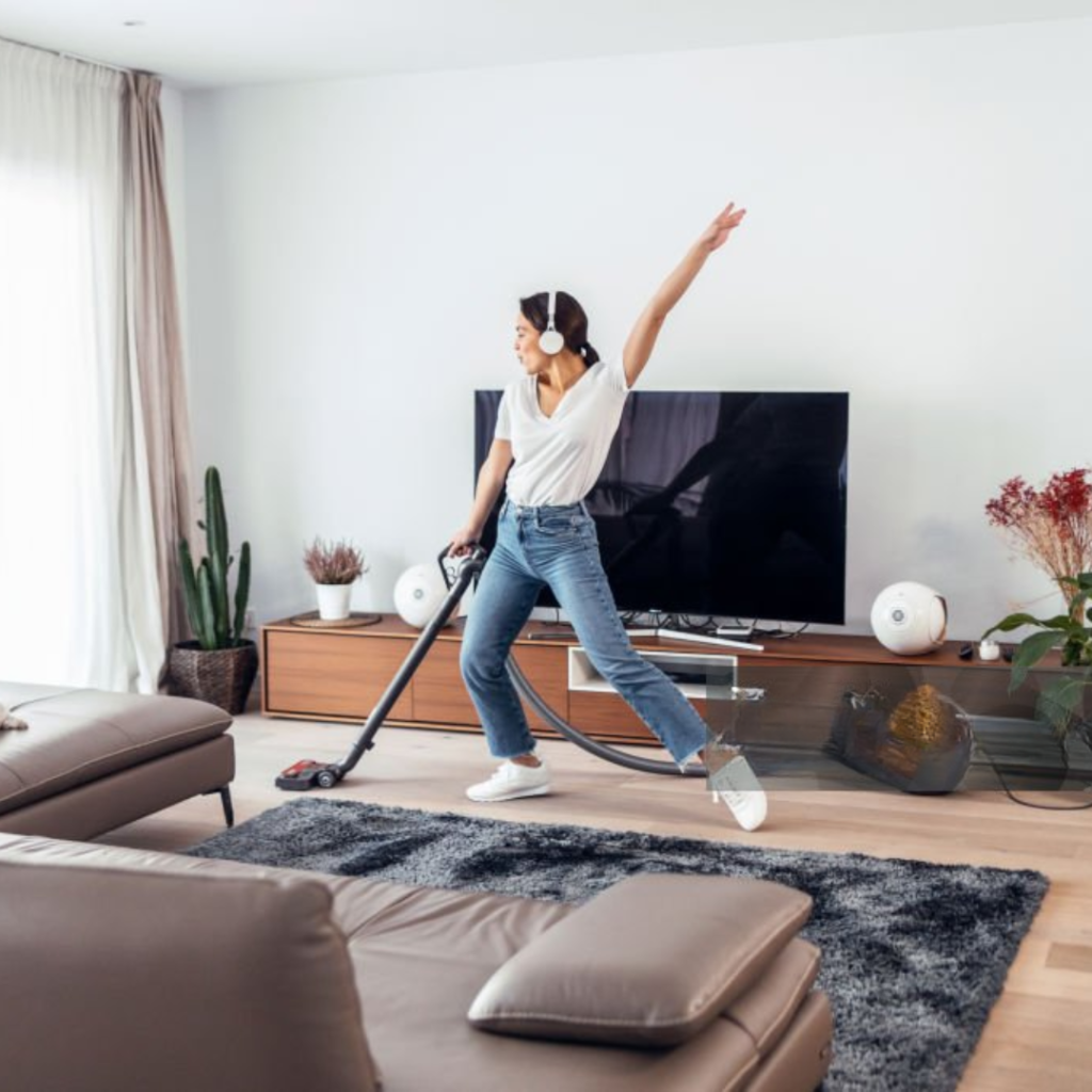 Young happy woman listening and dancing to music while cleaning the living room floor with a vaccum cleane